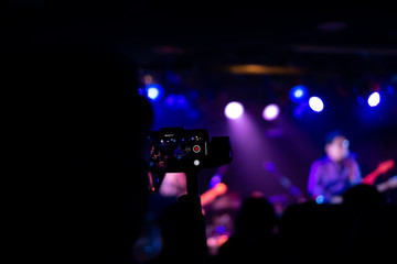 Fototapeta na wymiar Silhouette of hands using smart phone to take pictures and videos at live concert; Smartphone records live music; Take photo in front concert stage