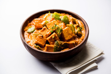 Malai or achari Paneer in a gravy made using red gravy and green capsicum. served in a bowl. selective focus