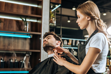 young hairdresser trimming beard to handsome client in beauty salon