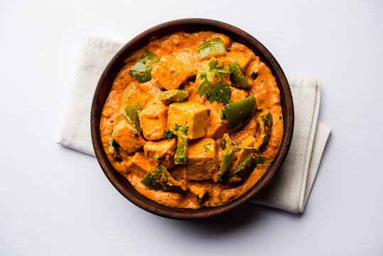Malai or achari Paneer in a gravy made using red gravy and green capsicum. served in a bowl. selective focus