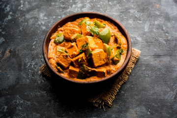 Malai or achari Paneer in a gravy made using red gravy and green capsicum. served in a bowl. selective focus
