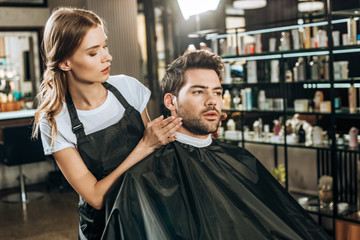 beautiful young hairdresser doing hairstyle to handsome male client in beauty salon