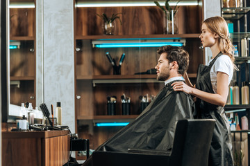 side view of female hairstylist and handsome young man looking at mirror in beauty salon