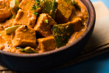 Malai or achari Paneer in a gravy made using red gravy and green capsicum. served in a bowl. selective focus