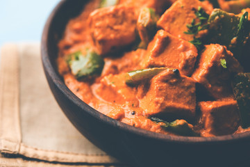 Malai or achari Paneer in a gravy made using red gravy and green capsicum. served in a bowl. selective focus