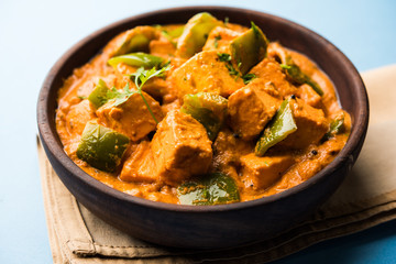 Malai or achari Paneer in a gravy made using red gravy and green capsicum. served in a bowl. selective focus