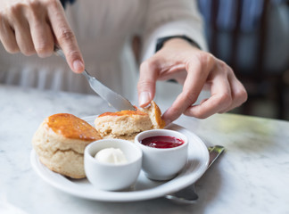 closeup hand of lady is cutting scone with jam