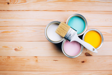 Four open cans of paint with brush on them on wooden natural background. Yellow, white, pink, turquoise colors. Top view.