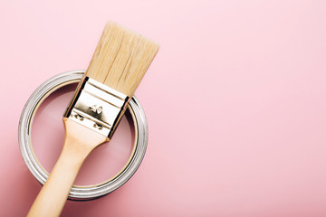 Brush with wooden handle on open can of pink paint on pastel background. Renovation concept. Macro.