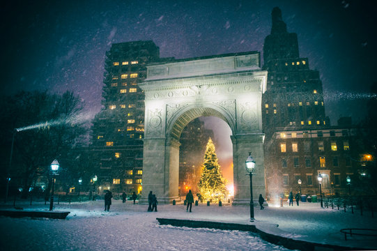 Winter holiday night view of the Washington Square Park with a Christmas tree under falling snow in New York City