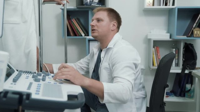 Phlebologist uses ultrasound machines to scan patient's veins on legs, steadicam shot.