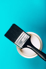 Brush with black handle on open can of white paint on blue background. Renovation concept. Vertical photo.