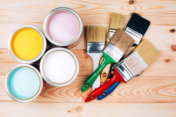 Four open cans of paint with brushes on natural wooden background. Yellow, white, pink, turquoise...