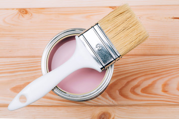 Brush with white handle on open can of pink color of paint on natural wooden board. Renovation...