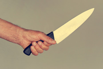 Hand of a male holding a knife isolated on a gray background . Close-up Big kitchen knife in man...