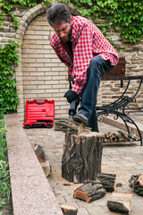 man in plaid shirt is sawing log with  electric saw