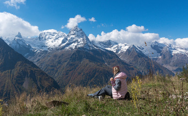 woman traveler drinks coffee with a view of the mountain landscape. A young tourist woman drinks a hot drink from a cup and enjoys the scenery in the mountains. Trekking concept.