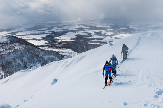 AERIAL: Three active tourists ski touring along the snowy mountain in Japan.