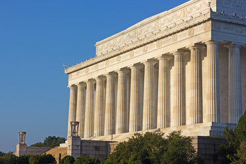 Fototapeta premium A little boy holding a book under armpit walks the steps of Lincoln Memorial in Washington DC, USA. Facade of Lincoln Memorial in the morning against a clear blue sky.