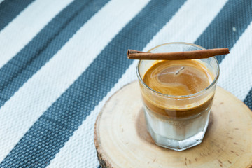 Coffee glass with cinnamon and wood coaster on tablecloth blue bar pattern background with copy space