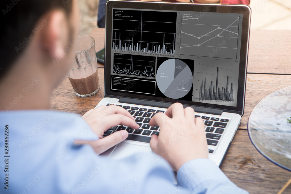 Poster back view of young businessman using laptop with stock chart data on screen.
