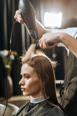 Cropped shot of hairstylist drying hair to beautiful young woman in beauty salon