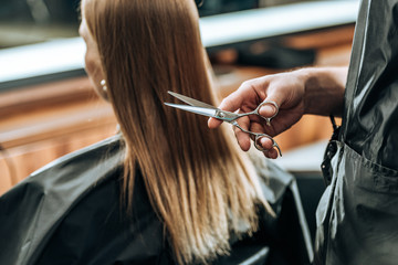 cropped shot of hairdresser holding scissors and young woman visiting beauty salon