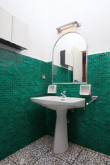 Sink and mirror in green tiled bathroom, old apartment interior
