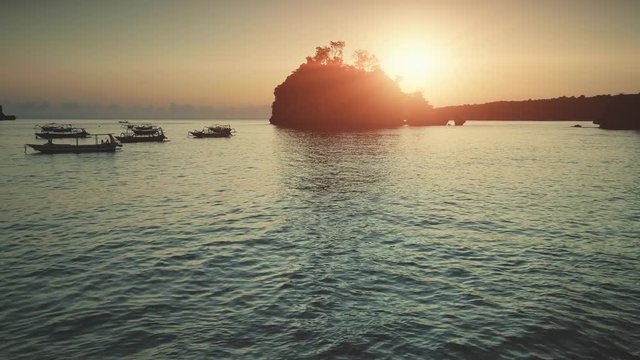 Sunset aerial view: Boats sailing in Ocean in soft orange light. Travel Vacation Recreation Paradise Tourism. Beautiful nature landscape in Tropical Nusa Penida Bali Island, Indonesia. 4K shot