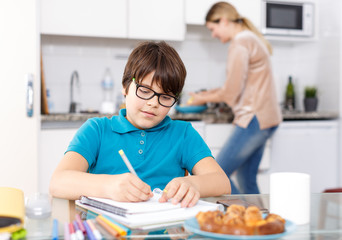 Obraz na płótnie Canvas Boy doing homework, mother cooking