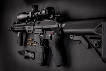 modern automatic rifle with an optical sight lies on a dark background and next to the knife and ammunition