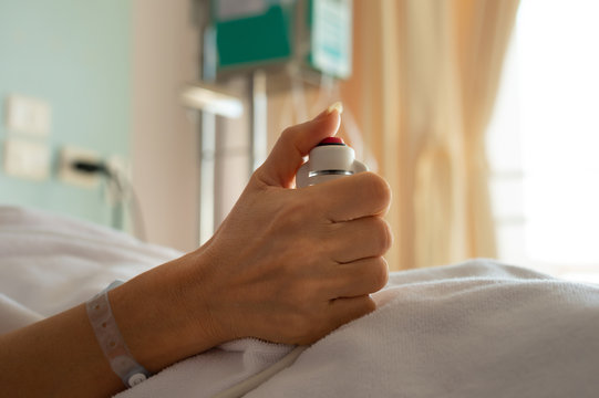 Hand holding  nurse call button,selective focused..Woman patient  in hospital dress under white blanket holding red emergency call button while lying in  bed.