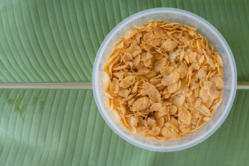 Corn flakes on plastic bowl with green banana leaf background