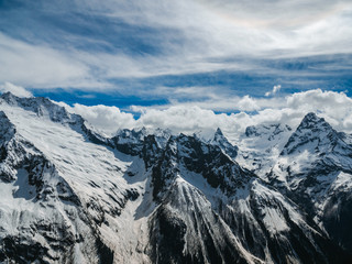 Mountain peaks covered with snow. Sunny day in the snowy mountains. Clouds above the mountain tops. Beautiful mountain background