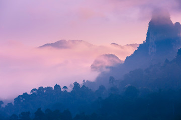 Pink dawn in the exotic mountains of Asia. Dawn on the lake in Thailand. The jungle covers the mountain peaks. Clouds float over the mountains.