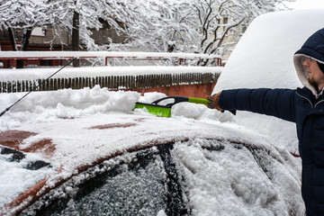 Young man cleaning his car from snow with brush