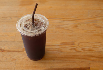Americano iced coffee in takeaway plastic cup on wooden desk in coffee's shop