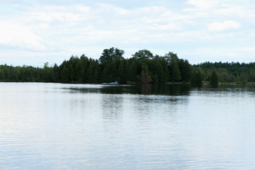 A husband and wife are in their boat on a beautiful lake. The sky is sunny and clouds are scattered.