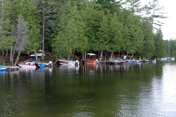 Boats are docked on a piece of land near a treeline just off of a lake.