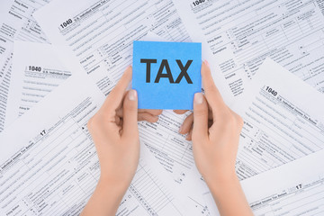 Obraz premium cropped view of woman holding blue card with word 'tax' and documents on background