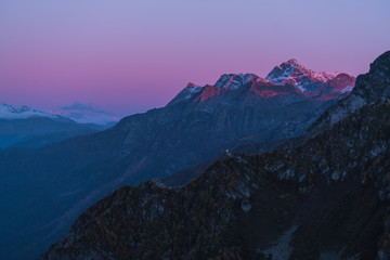 Fototapeta na wymiar Mountains in the sunset light. Purple peaks and dark blue sky. The sun's rays illuminate the tops of the mountains. Snow on mountain peaks