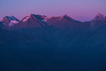 Plakat Mountains in the sunset light. Purple peaks and dark blue sky. The sun's rays illuminate the tops of the mountains. Snow on mountain peaks