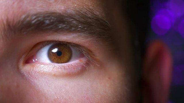 Closeup of male brown wide opened eye in an excited state looking straight at camera on the background ogf night lights