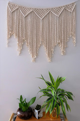 A large macrame wall hanging home decoration. Hand-made from 100% cotton rope. A wine rack and plants are used as props in decorating.