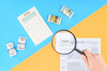 cropped view of woman holding magnifying glass over tax form on blue and yellow background