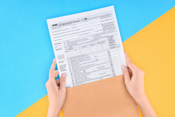 Obraz premium cropped view of woman holding tax form on blue and yellow background