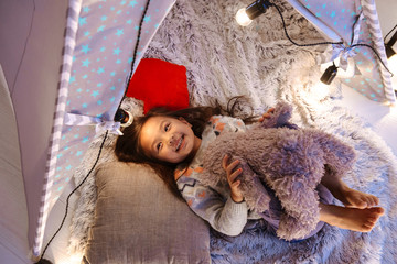 Photo of lovely asian little girl smiling, while lying with toys in children playing tent at home