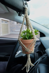 A mini jute twine macrame plant hanger with a ceramic pot. This hanger has a faux (Fake) plant inside of it. This hanger is made as a car decoration / charm. Side View.