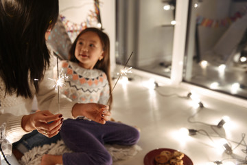 Happy young asian woman with her little daughter girl sitting on floor holding bengal lights. Christmas concept.
