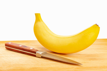 A fresh banana with a knife is lying on a wooden board. The background is white, isolate.